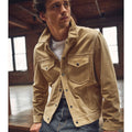 A man wearing a cream brown suede leather shirt jeans style jacket with a crew neck and zip closure, featuring outer pockets and inner pockets.