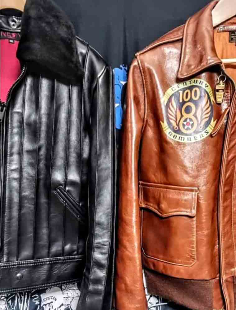 Two leather jackets displayed side by side: a black leather jacket with a dark fur collar on the left, and a brown leather jacket with a circular '100 Bombers' patch on the chest on the right.