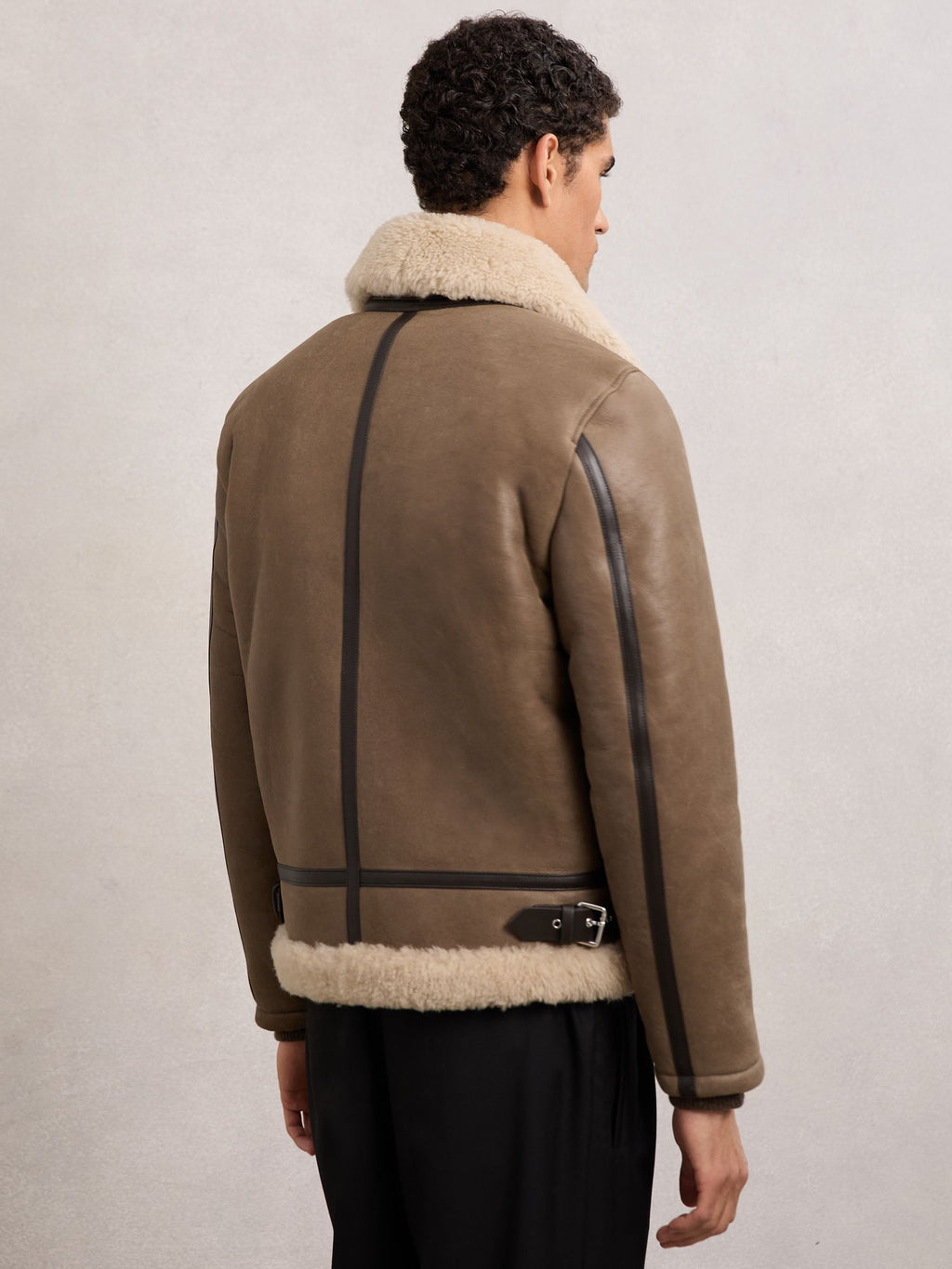Back of light brown shearling jacket with leather piping and waist buckle