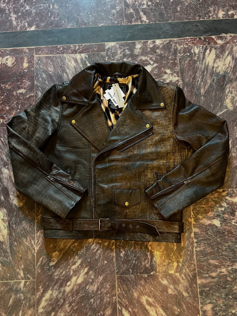 A black distressed leather motorcycle jacket with a matching belt, laid flat on a brown and gold marble-patterned tile floor.