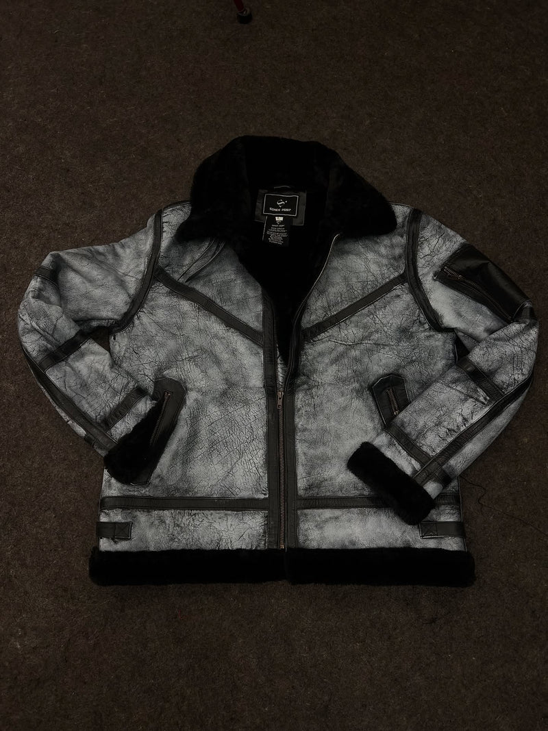 A gray and black faux-leather jacket with a black genuine shearling collar, laid flat on a dark brown carpet.