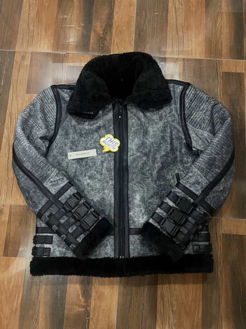 A gray and black textured jacket with black faux fur trim, laid flat on a wooden floor. It features a black zipper, black grid-patterned sleeve details, and a small yellow and white patch on the left chest.