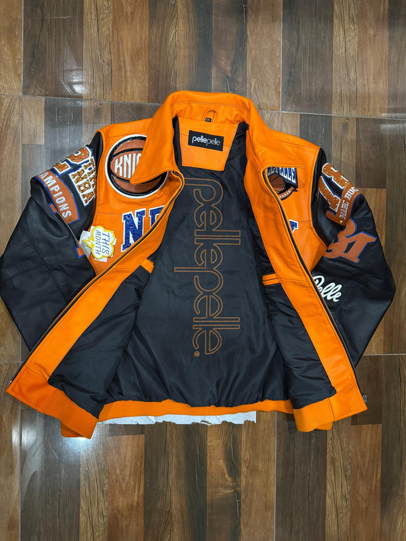 A black and orange PellaPella racing jacket laid flat on a dark wood floor, featuring various sponsor patches and logos.