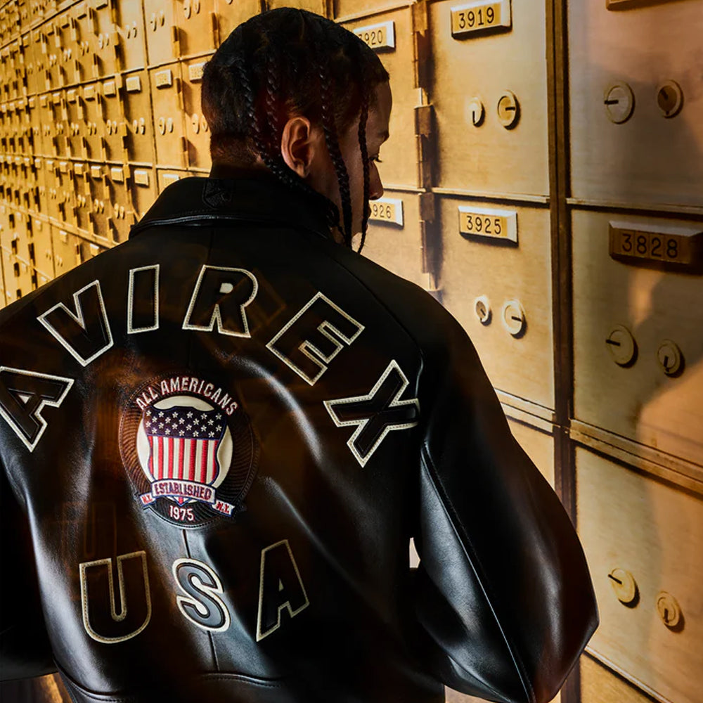 Person wearing a black leather jacket with 'AVIREX USA' branding in front of a gold safe deposit box wall.