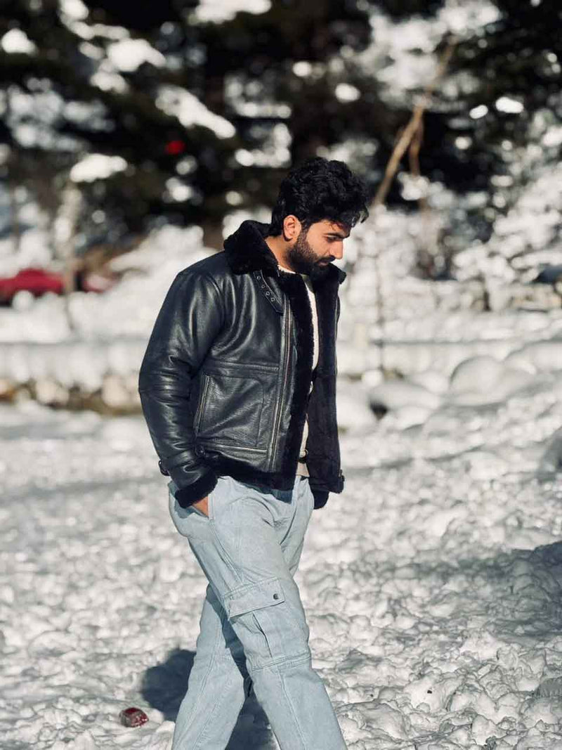 Person wearing a black leather jacket with fur trim in a snowy landscape