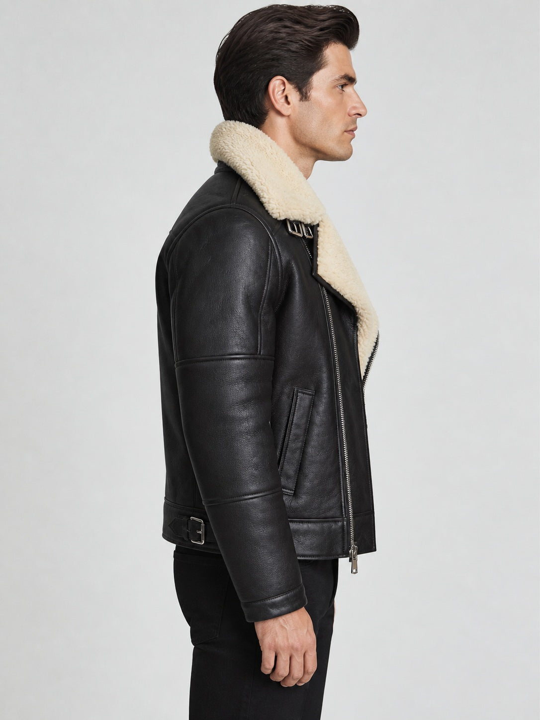 Side view of men’s black shearling aviator jacket showing angled welt pocket, sleeve panels and straight cuff