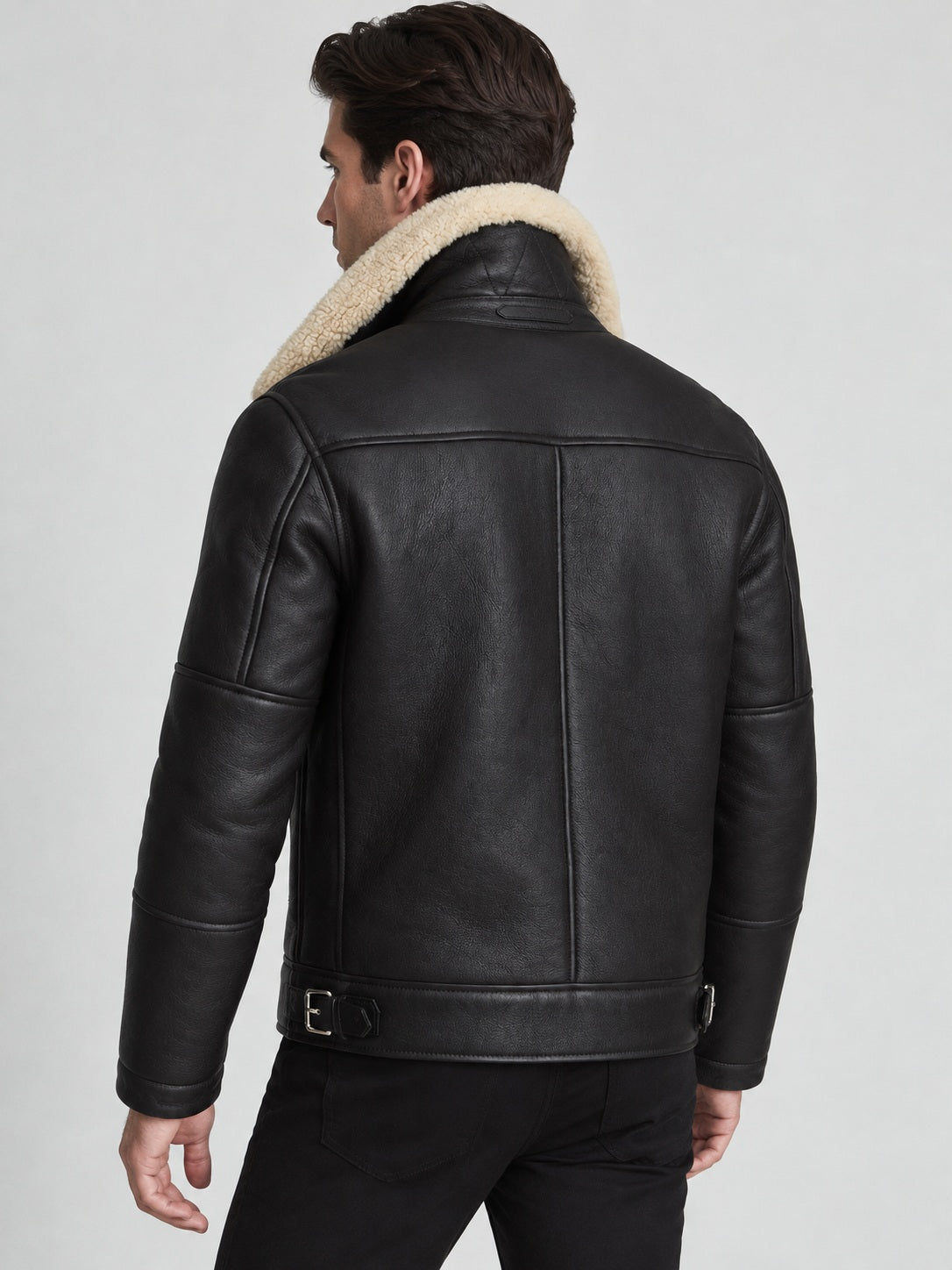 Three-quarter rear view of black sheepskin shearling jacket with panel stitching and silver-tone side buckles