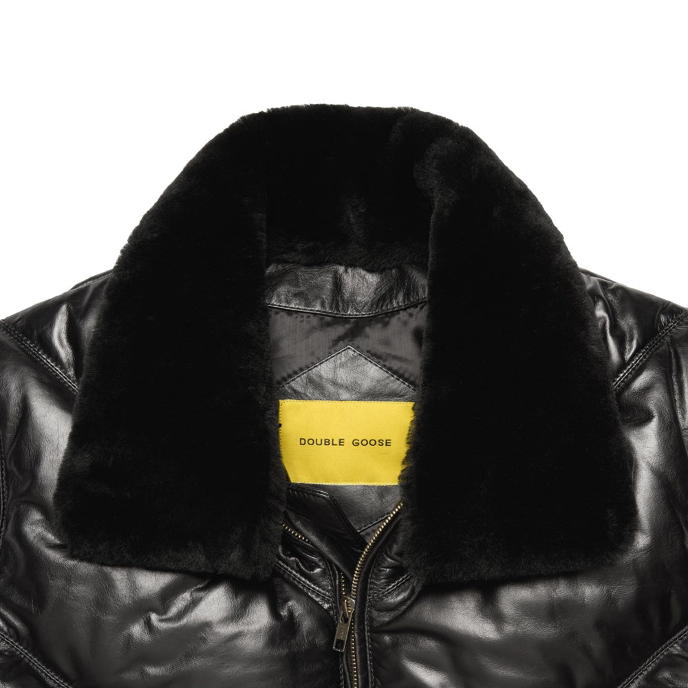 Close-up of a black leather bomber jacket with a thick black shearling collar and a yellow Double Goose neck label, shown against a plain white background.