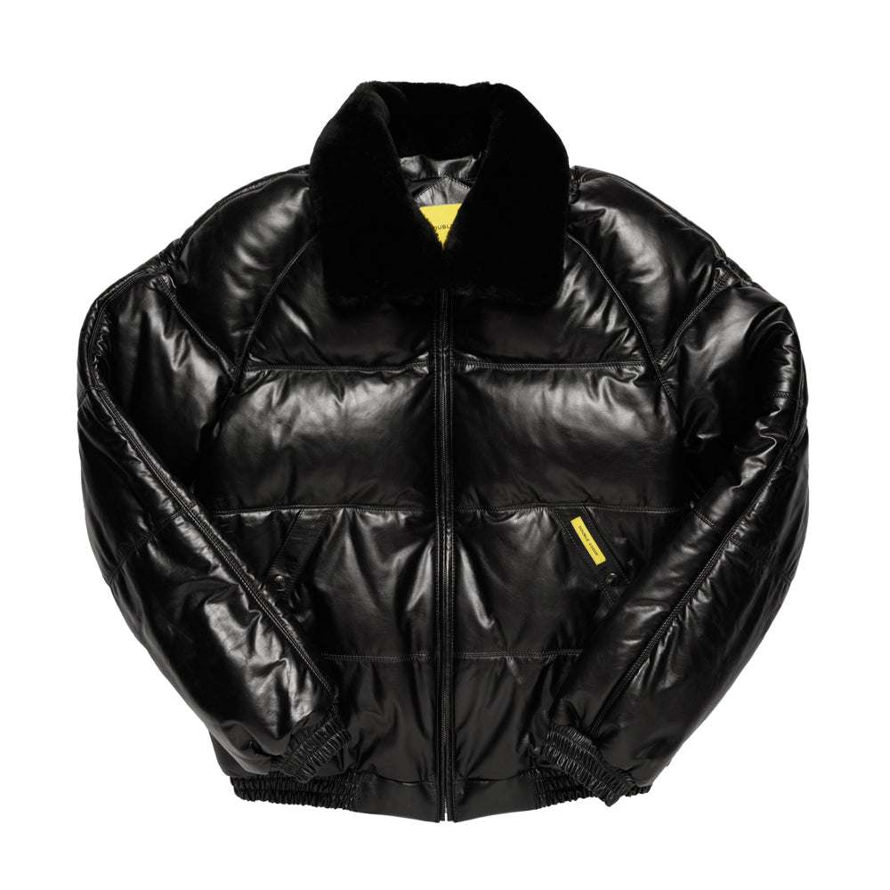 A black puffer jacket with a glossy, patent-like finish, featuring a black fur collar, a front zipper closure, and small yellow accent tabs on the chest.