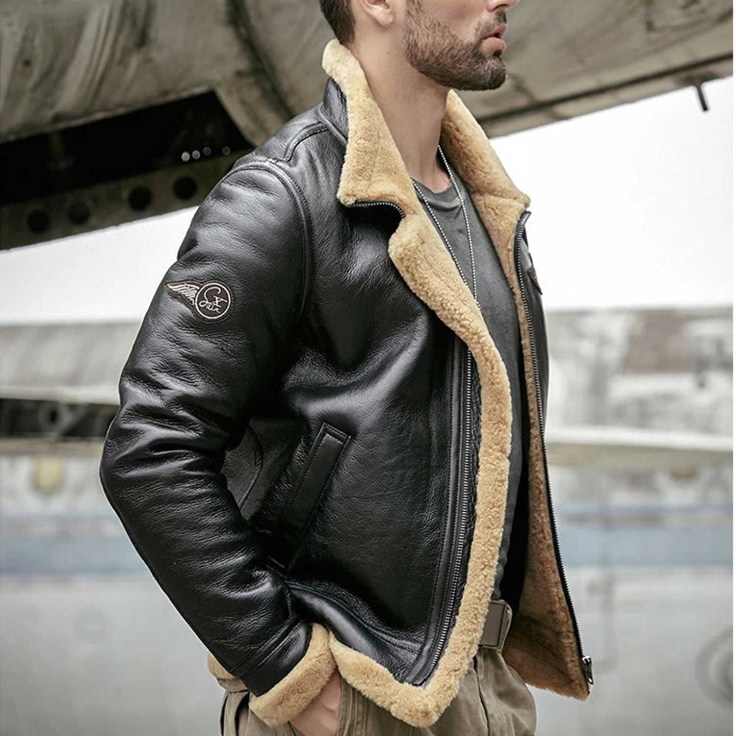 A man wearing a black leather aviator-style jacket with a thick beige shearling lining, standing in front of a blurred industrial background.