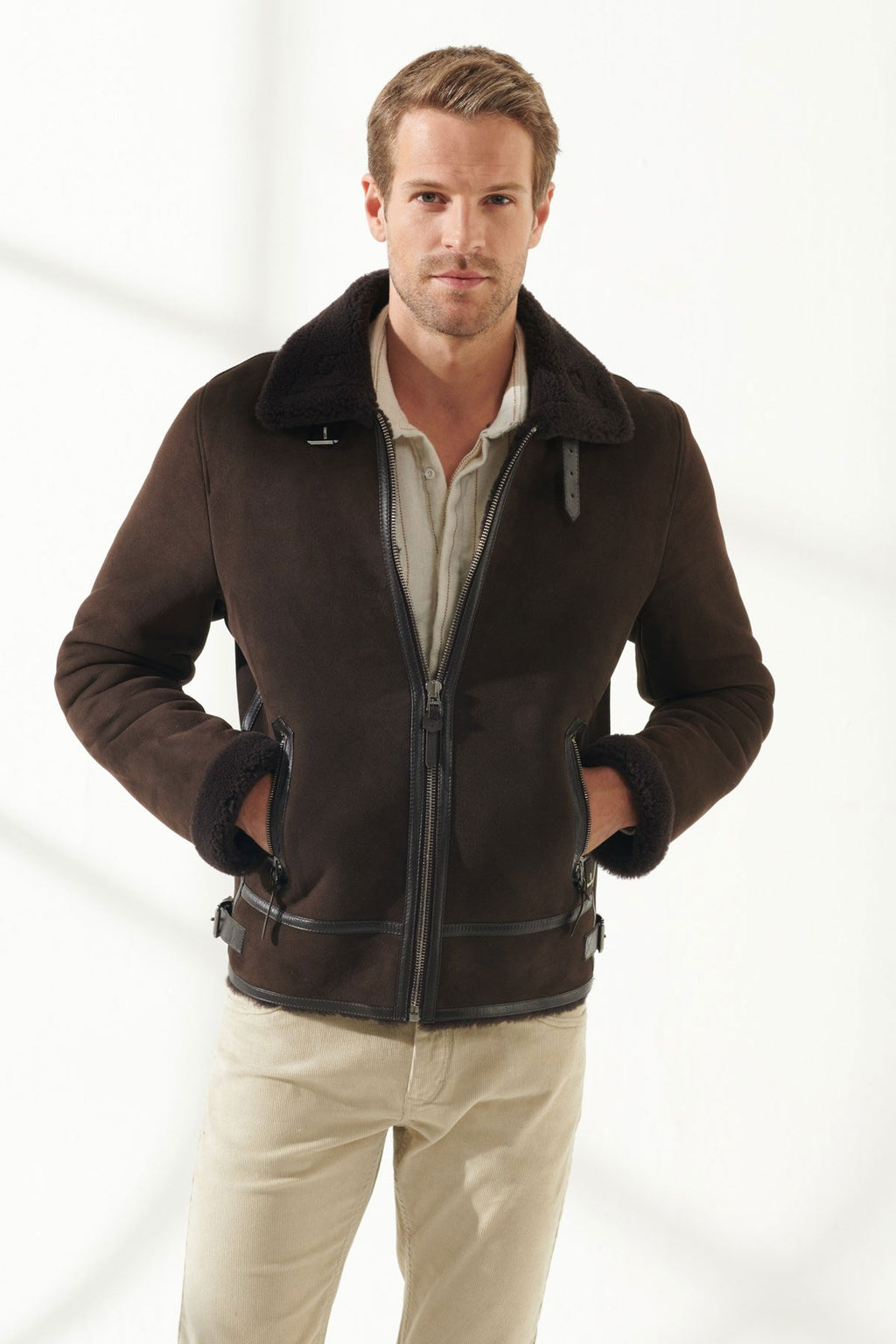 A man wearing a brown aviator shearling jacket with a standing collar, zipper details, and a casual fit.